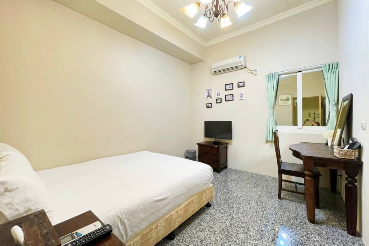 A hotel room with a bed, a desk, a chair, a television, and a wall-mounted air conditioner.