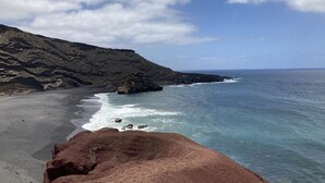 Un paysage côtier avec une plage rocheuse, une mer d’un bleu limpide et une vue lointaine sur l’océan.