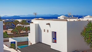 Une terrasse sur le toit avec une piscine, des murs blancs et une vue dégagée sur la mer et les montagnes.
