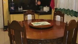 A dining area with a wooden table and chairs, a kitchen in the background, and a clock on the wall. - Pines Mansion II House (Butuan)