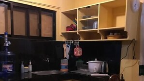 A compact kitchen with yellow cabinets, a black countertop, and a dining table. - Pines Mansion II House (Butuan)