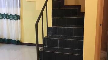 A staircase with black tiles and a metal handrail, leading to a room with yellow walls and a white curtain with green trim.