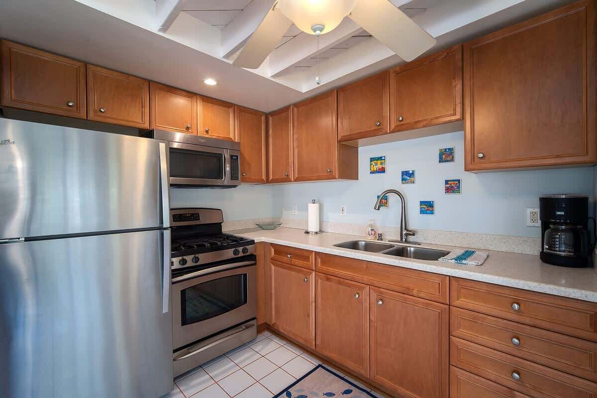 A kitchen with wooden cabinets, stainless steel appliances, a tiled floor, and a ceiling fan.