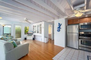 A spacious living area with a grey sofa, wooden flooring, and a kitchen with stainless steel appliances.