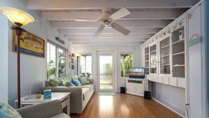 Ein geräumiges Wohnzimmer mit Holzboden, Deckenventilator, Fernseher und Bücherregal.