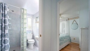Ein Badezimmer mit Dusche, Toilette und Waschbecken sowie ein Schlafzimmer mit Bett und Kommode.