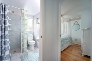 Un bagno con doccia, toilette e lavandino, e una camera da letto con un letto e una cassettiera.