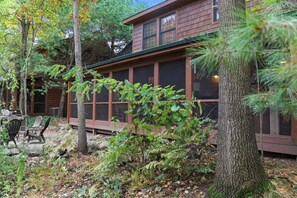 Une cabane dotée d’une terrasse, entourée d’arbres, et comprenant un espace patio aménagé avec du mobilier d’extérieur.