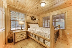 Une chambre à coucher dans un chalet en bois, avec un lit, une table de chevet, une lampe et une fenêtre avec des stores.