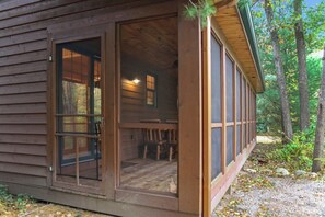 A wooden cabin with a large sliding door, a small porch, and a view of the surrounding forest.