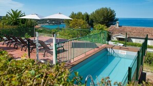 A pool area with lounge chairs and umbrellas, surrounded by greenery and overlooking a body of water. - La Maison de l'Amiral by Interhome (Sanary sur Mer)