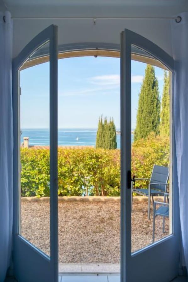 A room with a large circular window offering a view of the sea, a vineyard, and a chair.