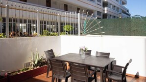 Una terraza en la azotea con una mesa y sillas, rodeada de plantas en macetas.