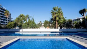 Una piscina con agua azul cristalina, rodeada de palmeras y edificios.