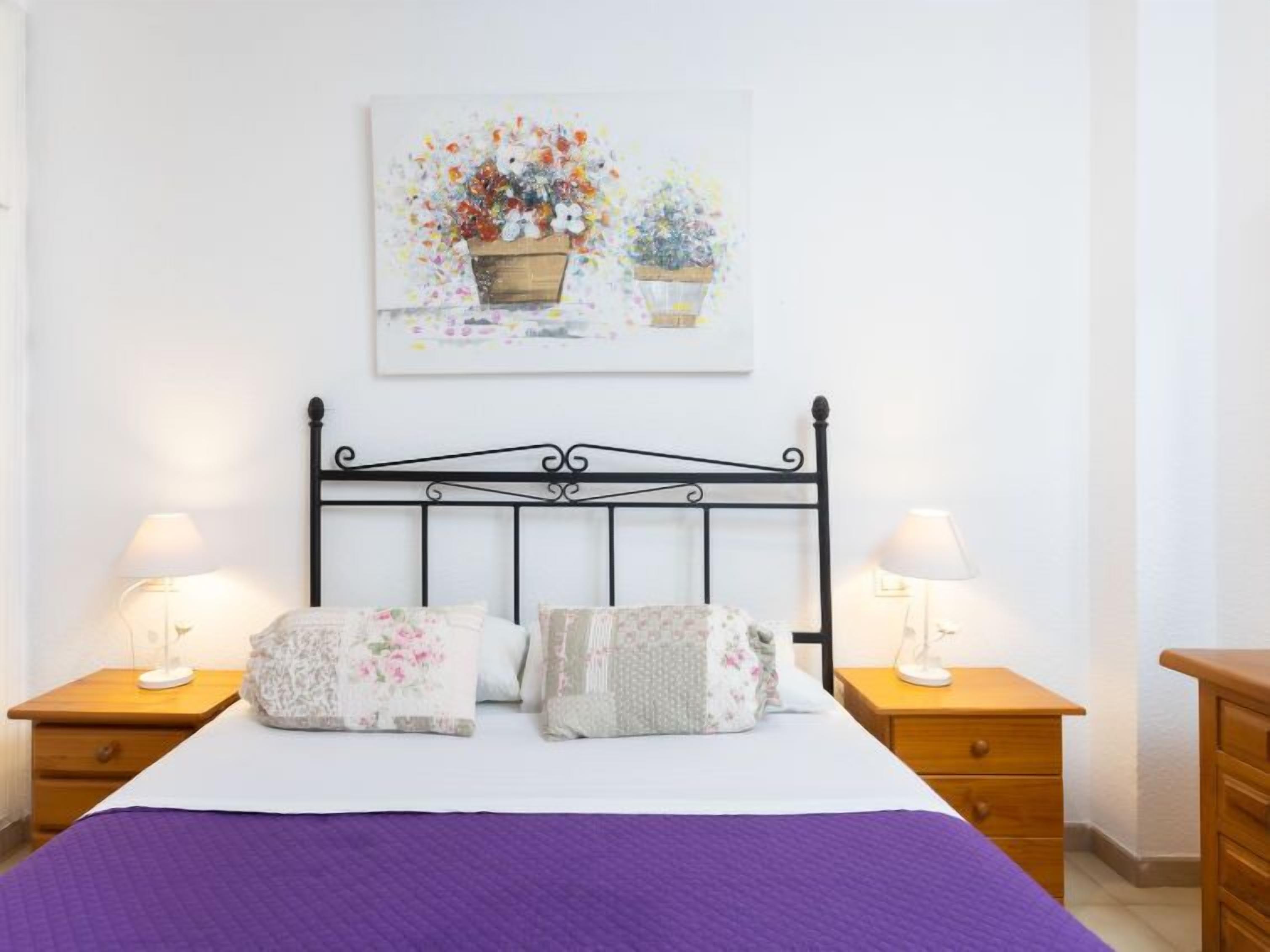 Ein ordentlich eingerichtetes Schlafzimmer mit einem Bett, zwei Nachttischen und einem Wandbild.