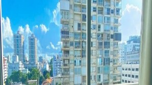 Un balcón con dos sillas, vista a un paisaje urbano con edificios altos y un cielo despejado.