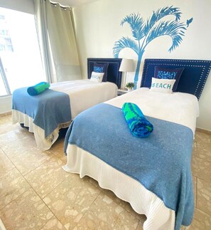 A hotel room with two beds, each with a blue and white bedspread and a blue towel.