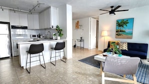 Una cocina moderna con electrodomésticos de acero inoxidable, un comedor con sofá azul, y un cuadro con una playa.