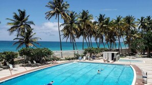 Una piscina con agua azul cristalina, rodeada de palmeras y vista al océano.