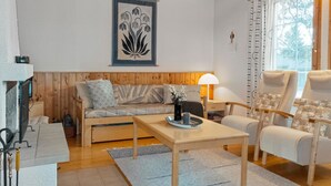 A cozy living room with a wooden sofa, a coffee table, and a chair. There is a painting on the wall and a window with curtains. - Siulapalkinen a 4 by Interhome (Inari)