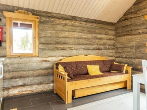 L’intérieur d’une cabane en rondins, avec un canapé en bois, une fenêtre et une chaise blanche.