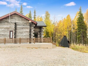 Une cabane en rondins avec une terrasse en bois et une cheminée noire.