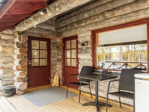 Una cabaña de troncos con fachada de madera, dos puertas de vidrio, una mesa de comedor con sillas y vista a árboles a través de una ventana.