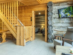 Un interior de madera con una escalera, un televisor fijado a una pared de tronco y un área de descanso con una mesa y sillas.