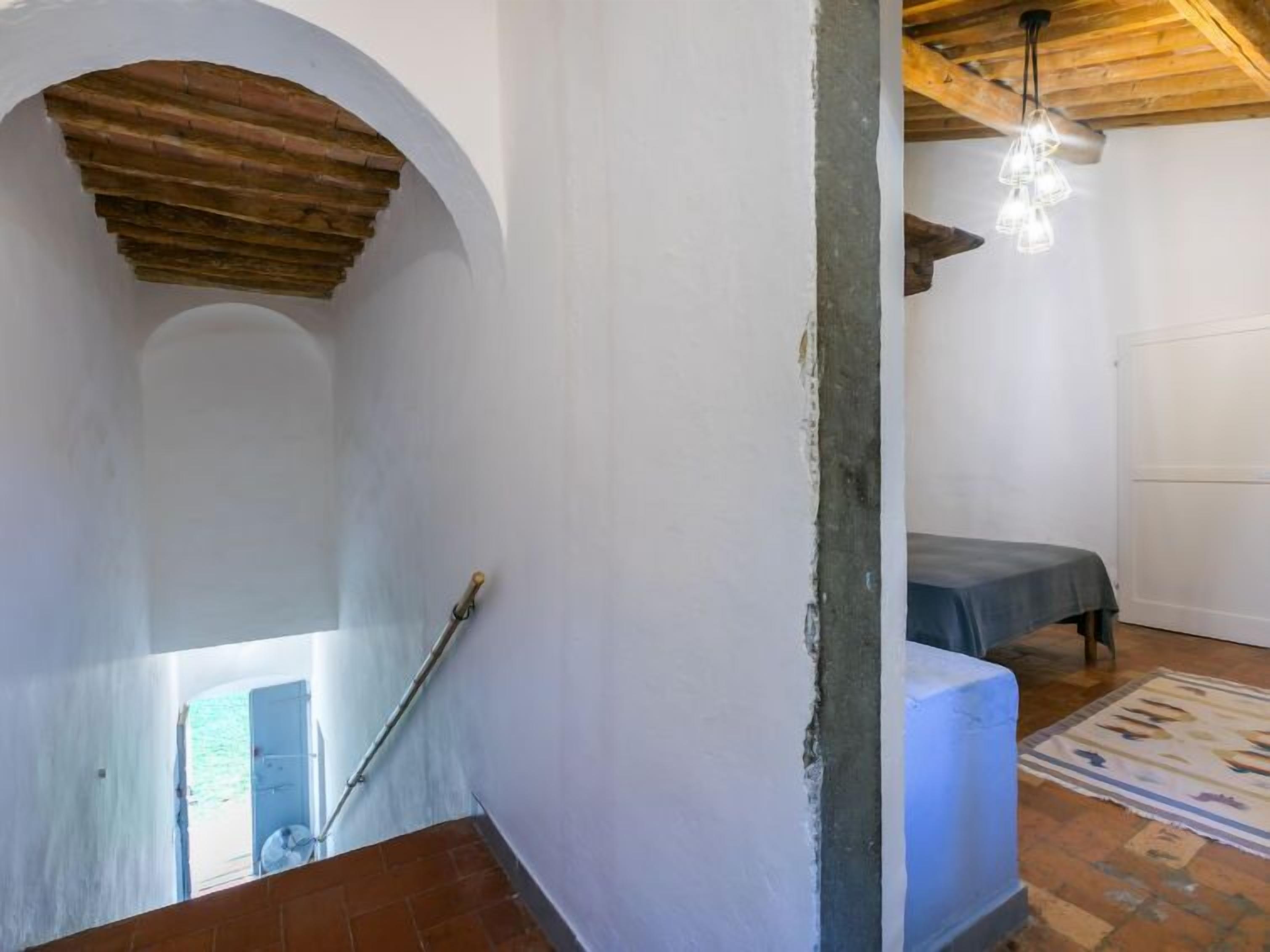 Une pièce avec un escalier, un lit, un luminaire suspendu et un tapis à motifs.