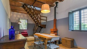 Un coin repas avec une table en bois, deux chaises, un vase bleu, une chaise rouge, un escalier et une fenêtre donnant sur un paysage verdoyant.