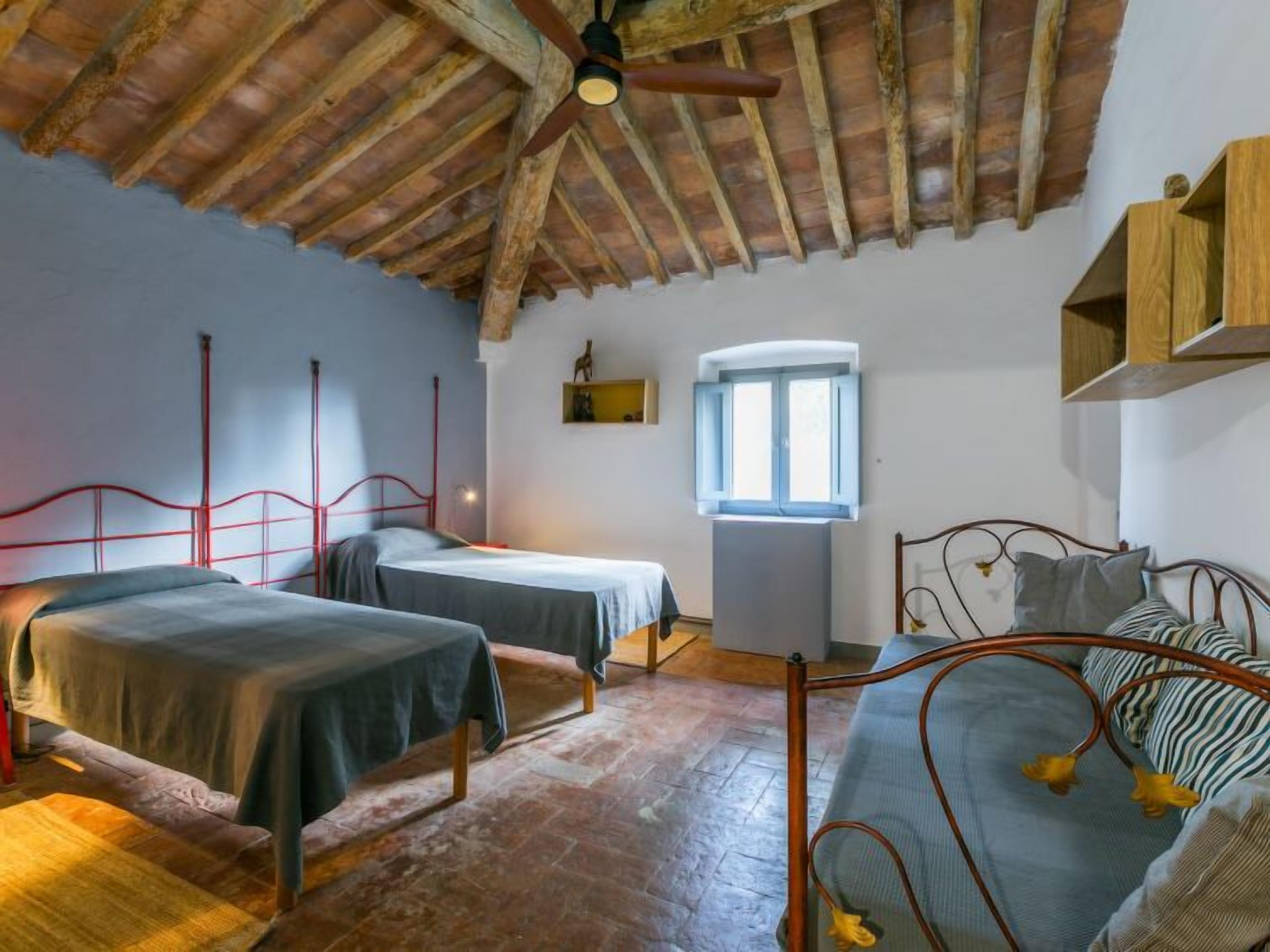 Une chambre avec deux lits, un plafond en bois, une fenêtre et une étagère intégrée.