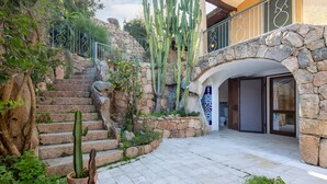A stone staircase leading to a covered entrance with a view of a courtyard featuring cacti and potted plants. - Valentina by Interhome (Cannigione)