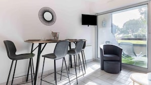 A modern dining area with a round table, four chairs, a TV mounted on the wall, and a large window offering a view of the outdoors. - Apartment Océan by Interhome (Carnac)