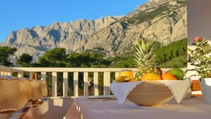 Une table avec des fruits et une bouteille sur un balcon donnant sur une vue sur les montagnes.