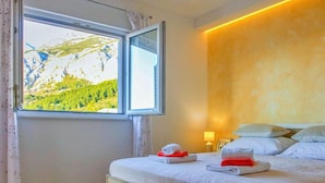Une chambre d’hôtel avec un lit, une fenêtre donnant sur les montagnes, une table de chevet avec une lampe et un mur à la finition texturée.