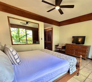 Une chambre à coucher comprenant un lit, une télévision, une commode et un ventilateur de plafond.