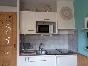 Une petite cuisine équipée d’un four à micro-ondes, d’un évier et d’une horloge murale.
