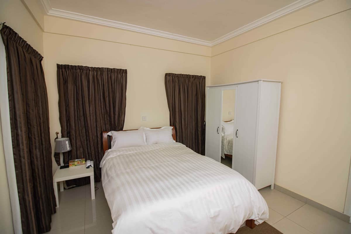 A hotel room with a bed, a nightstand with a lamp, and a wardrobe.