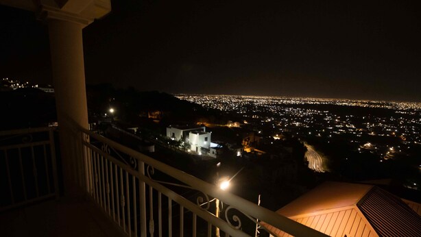 Una vista notturna da un balcone su un panorama urbano con edifici illuminati e un profilo cittadino in lontananza.