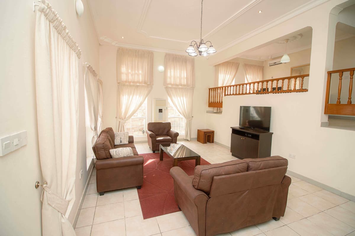 A living room with brown sofas, a coffee table, a TV, and a staircase with a wooden railing.