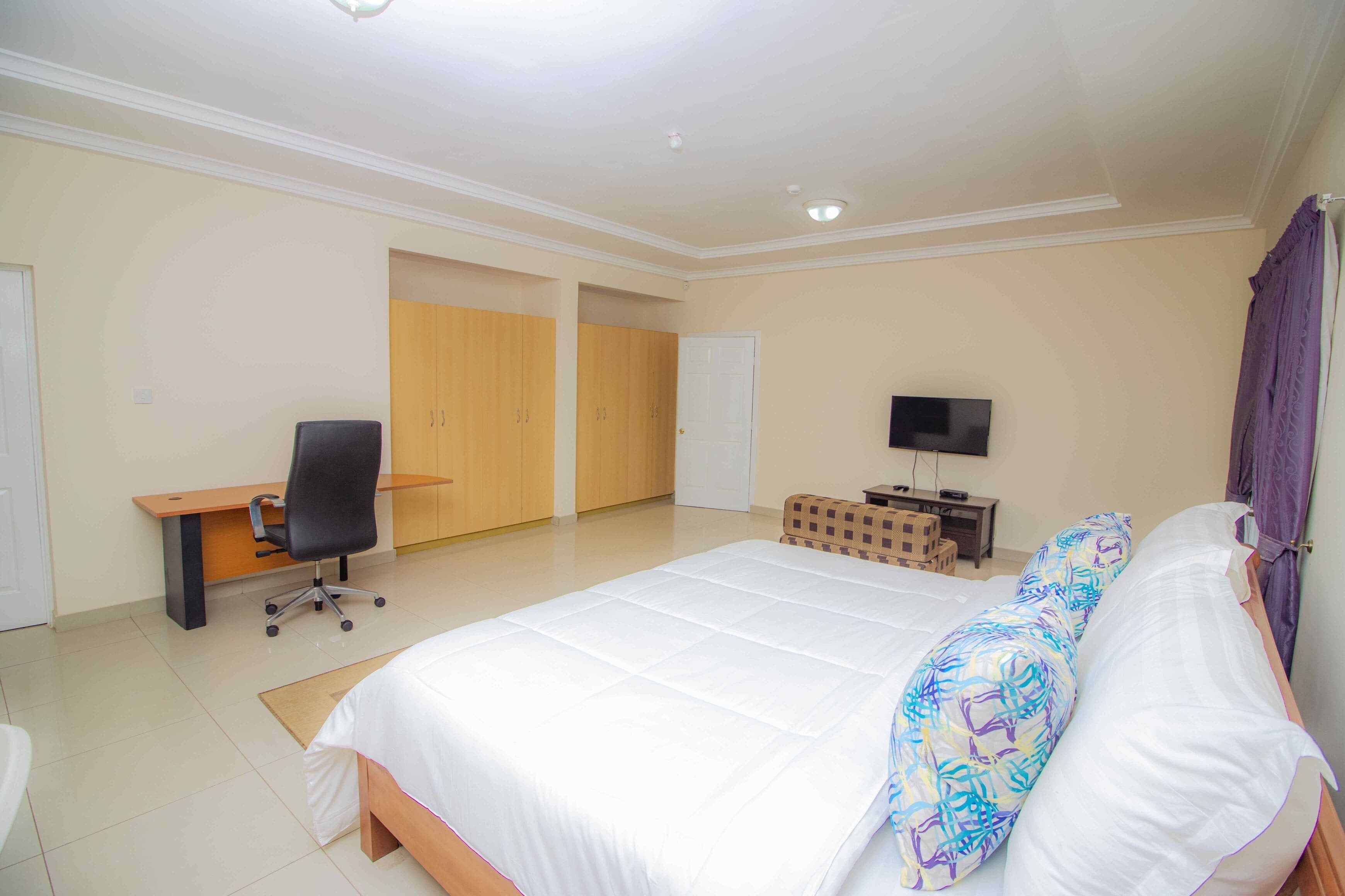A bedroom with a large bed, a desk, a chair, a television, and a wardrobe.