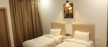 Ein Hotelzimmer mit zwei Betten, beigen Vorhängen, einem Buddha-Gemälde und einem Nachttisch mit Wasserflaschen.