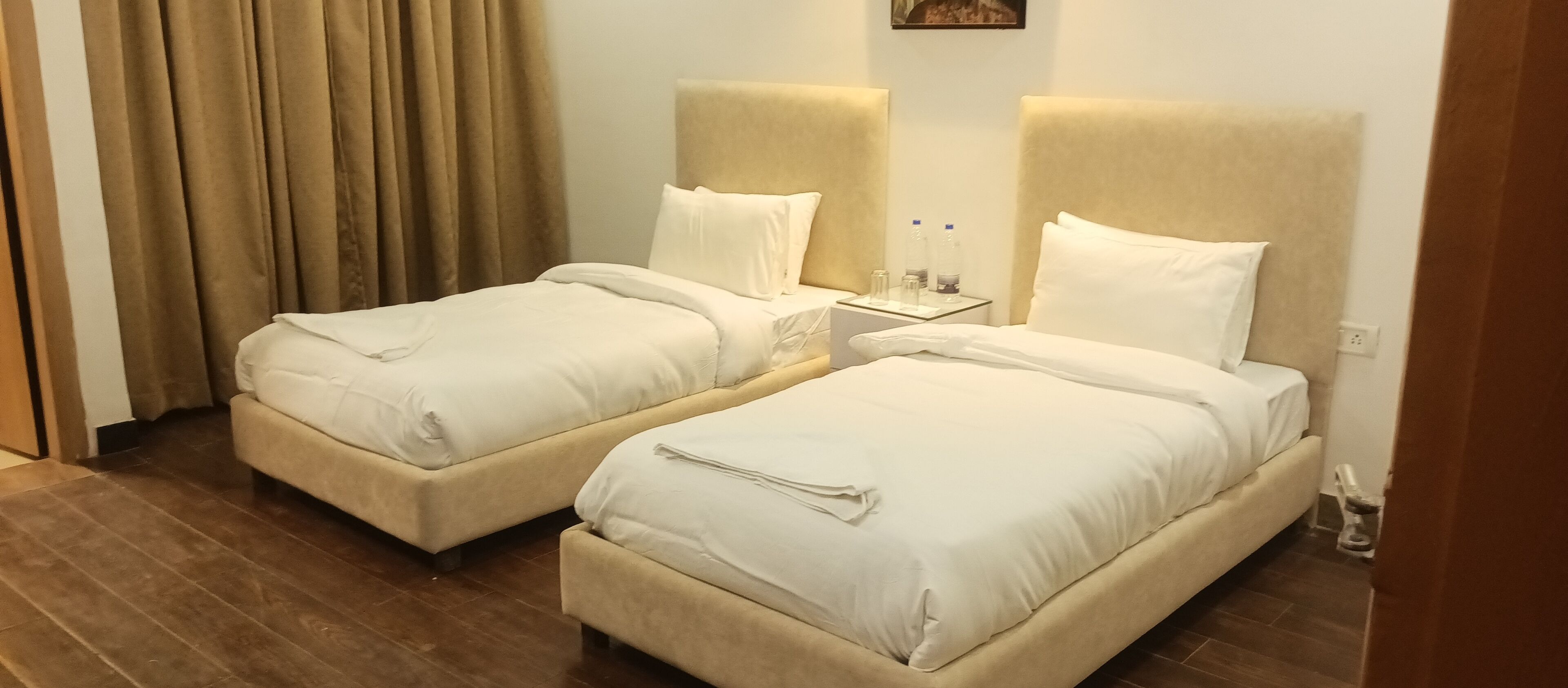 Habitación de hotel con dos camas individuales, una mesita de noche con lámpara y ventana con cortinas.