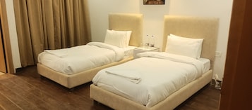A hotel room with two single beds, a nightstand with a lamp, and a window with curtains.