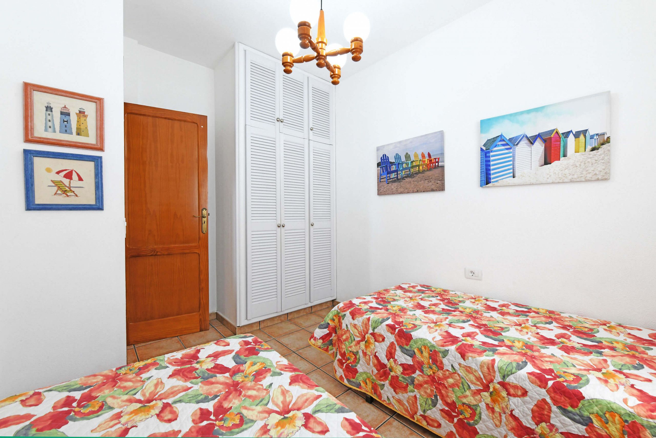 A bedroom with two single beds, a wooden door, a wardrobe, and a ceiling light fixture.