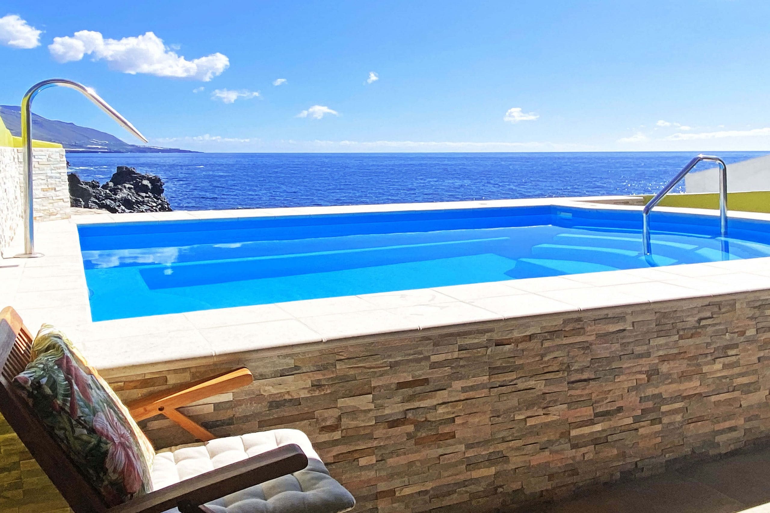 Una piscina con vista al océano, un muro de piedra y una silla.