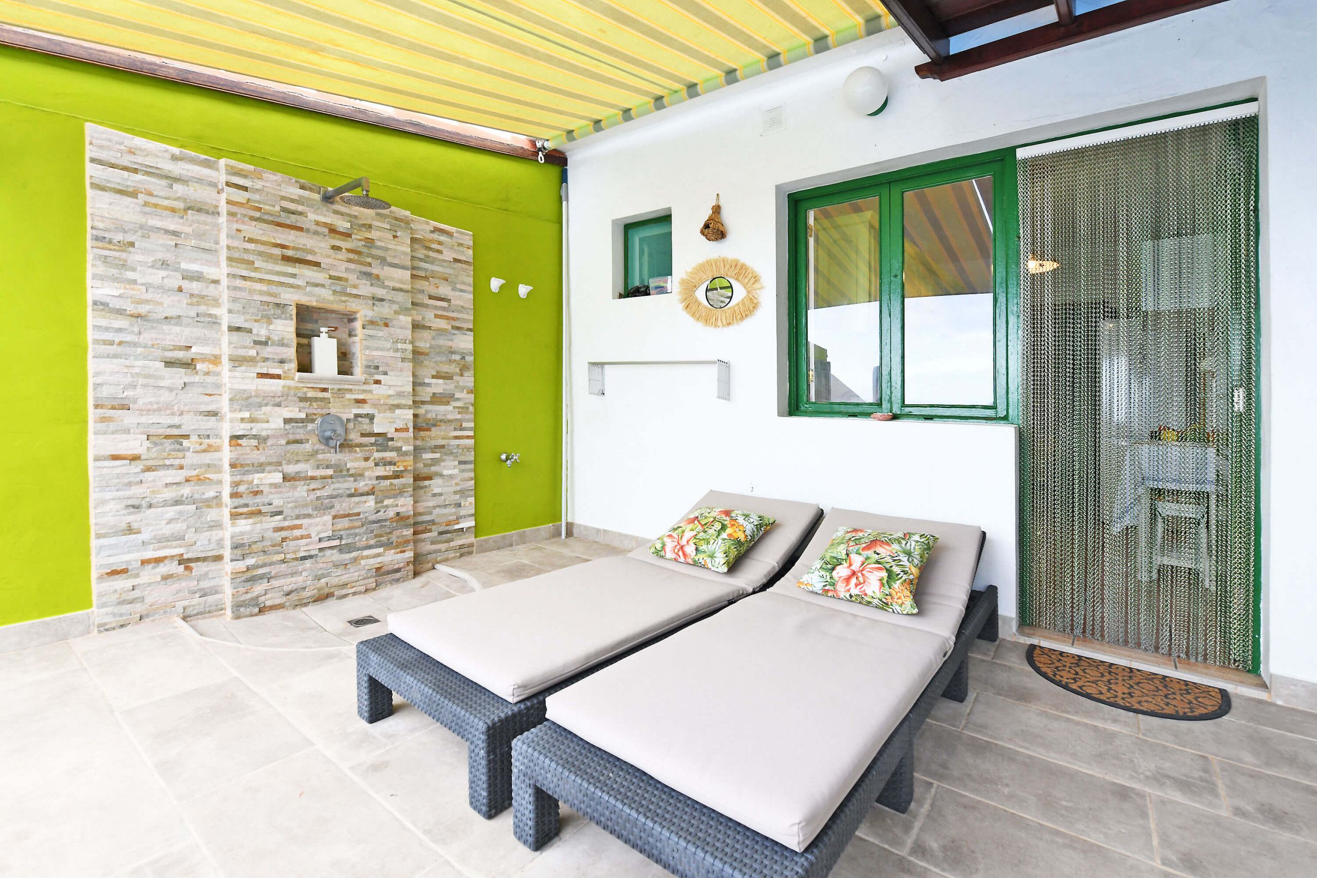 Quarto com duas camas, parede de pedra, porta verde e janela com moldura verde.
