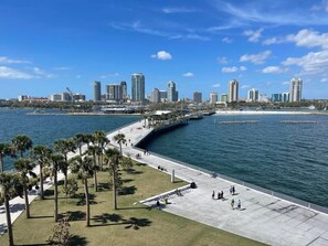 Eine Uferpromenade mit Stadtansicht im Hintergrund, darunter hoch aufragende Gebäude und ein klarer, blauer Himmel.