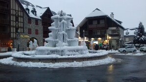 Ein mit Schnee bedeckter Brunnen auf einem Marktplatz, im Hintergrund sind Gebäude zu sehen.