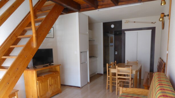 Ein kompakter Wohnraum mit einer Holztreppe, einem Essbereich, einer Couch und einer Küche.